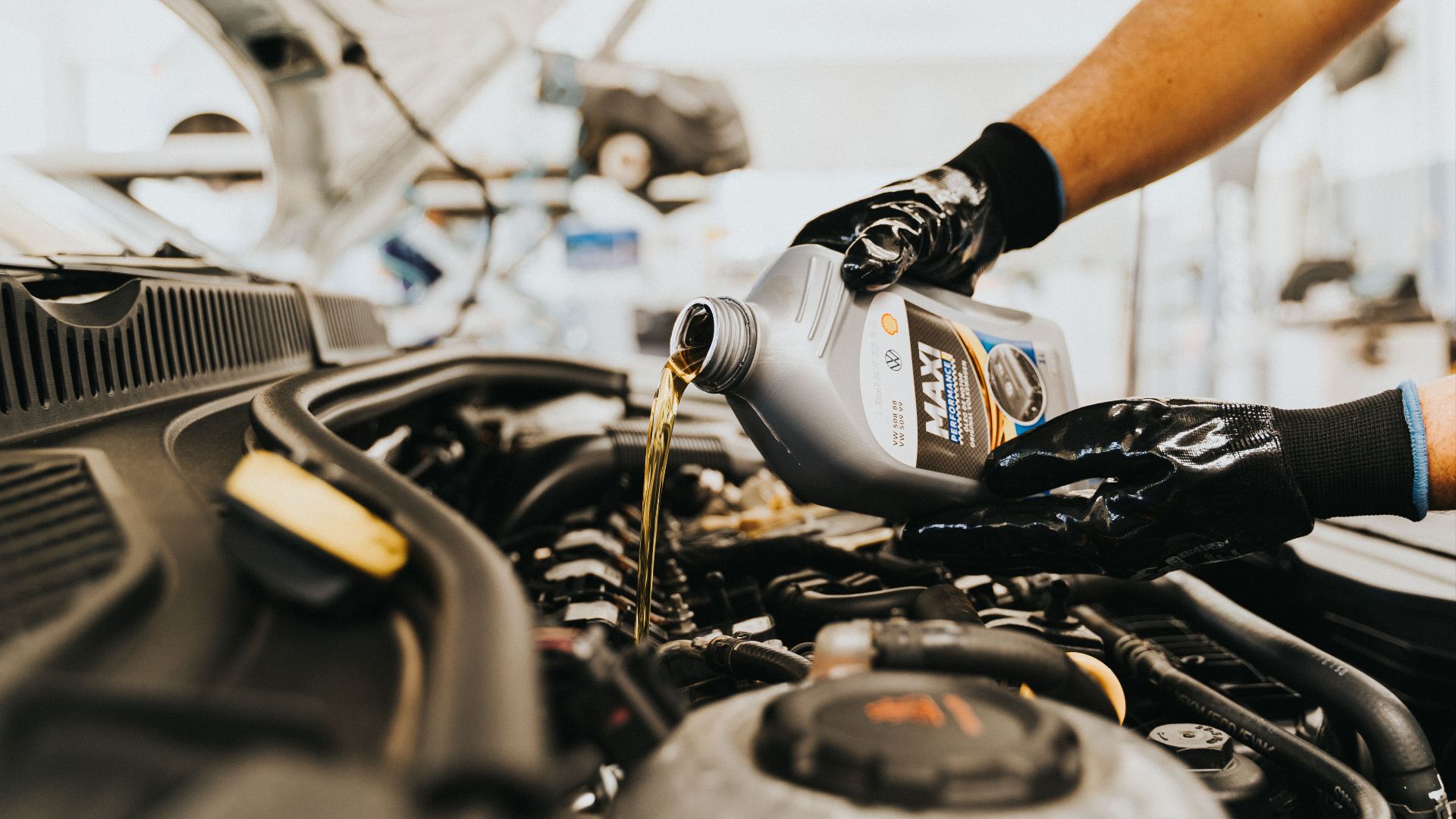 Close-up of a mechanic pouring engine oil into a car engine in an auto repair shop.