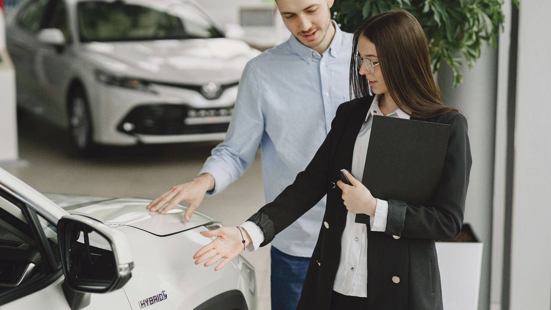 A man and saleswoman discussing a hybrid vehicle's features in an indoor showroom.