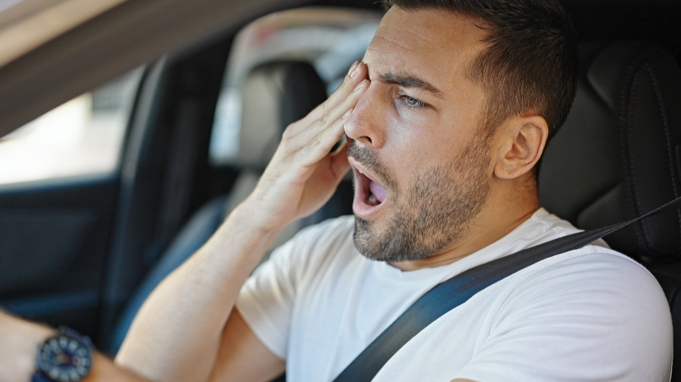 Tired man driving car and yawning at street.