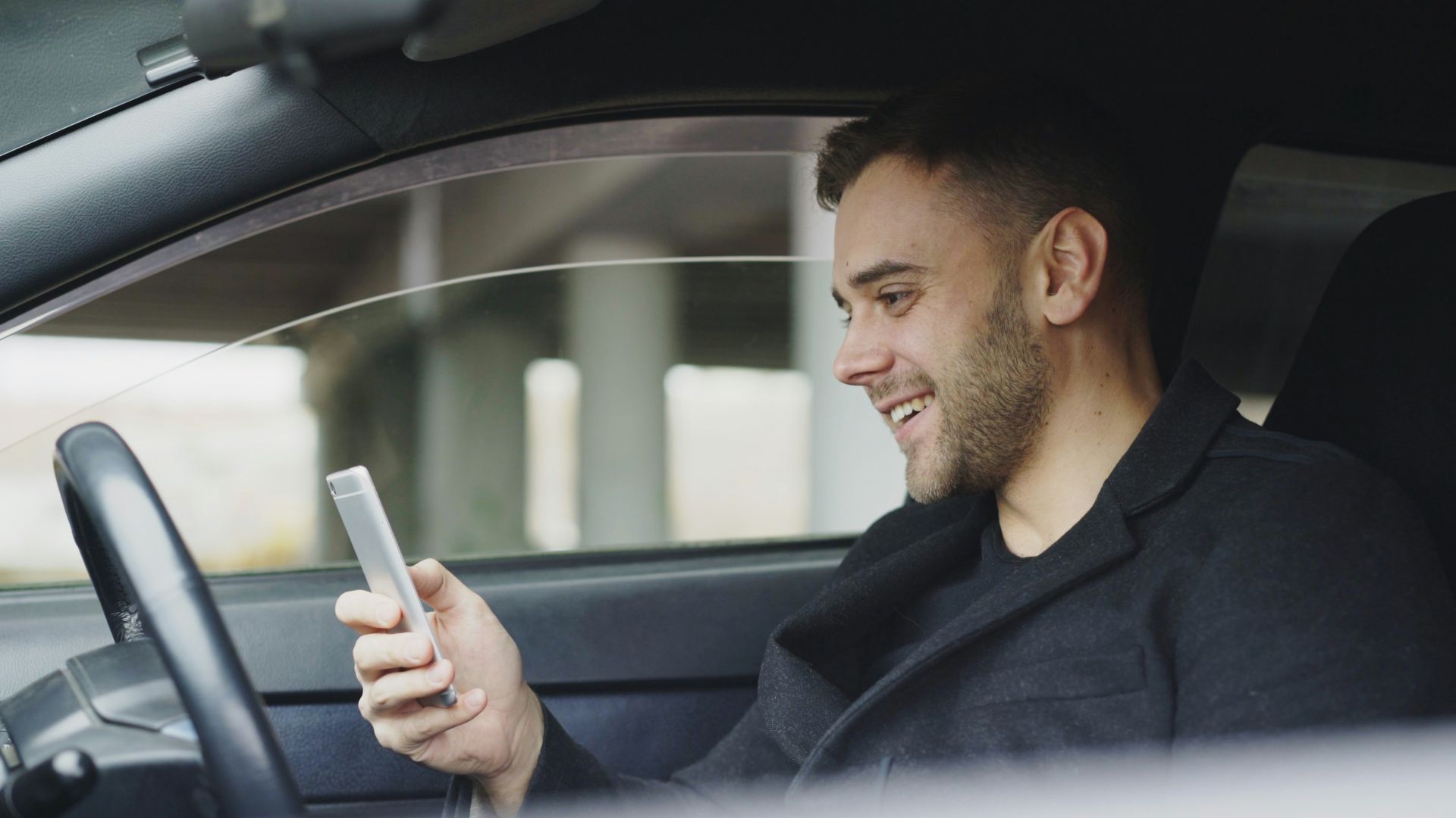 Man smiling while looking at his phone in car