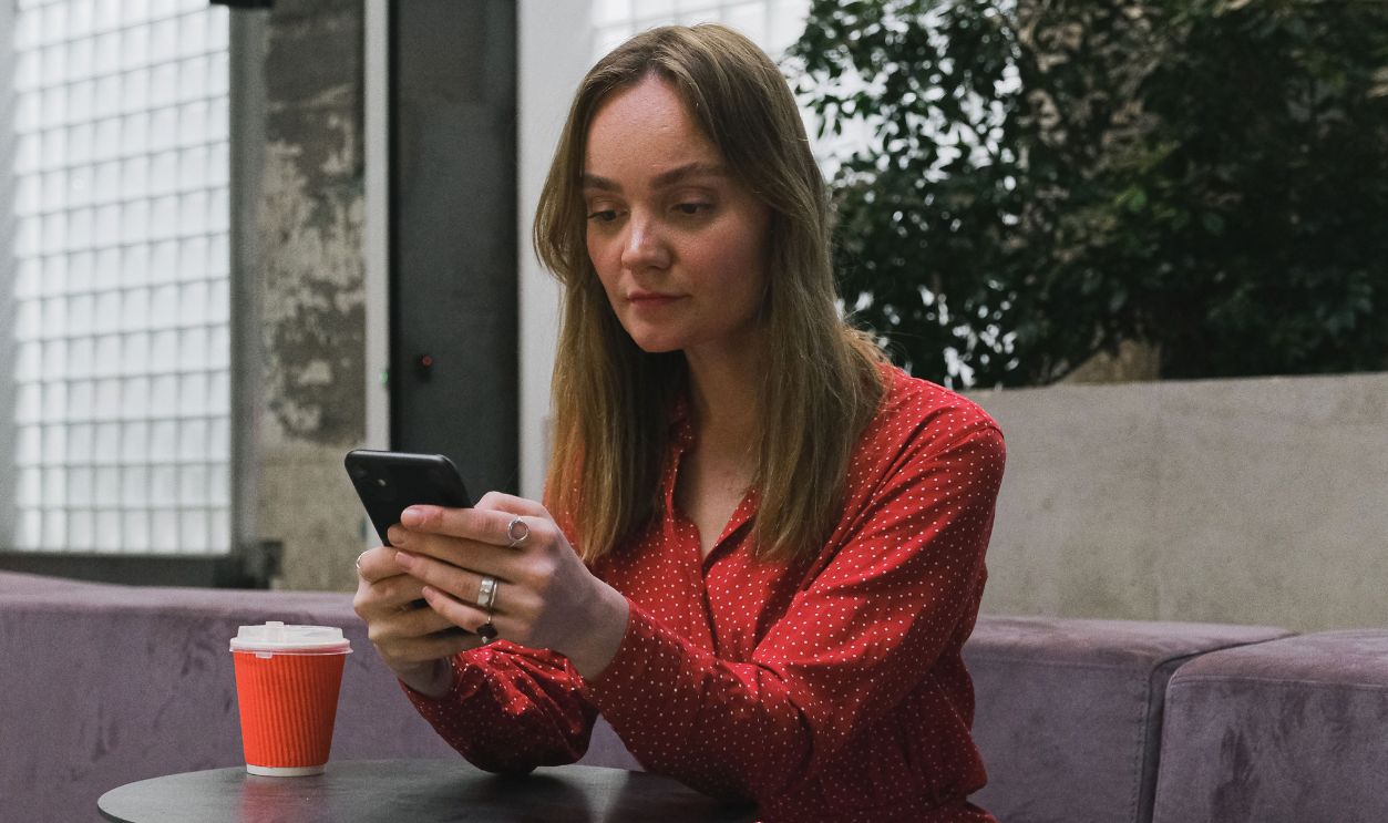 Young woman in red dress sitting indoors, using smartphone at a table 