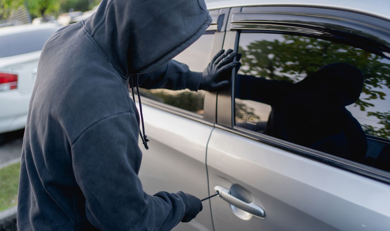Robber breaking into a car at the parking lot.