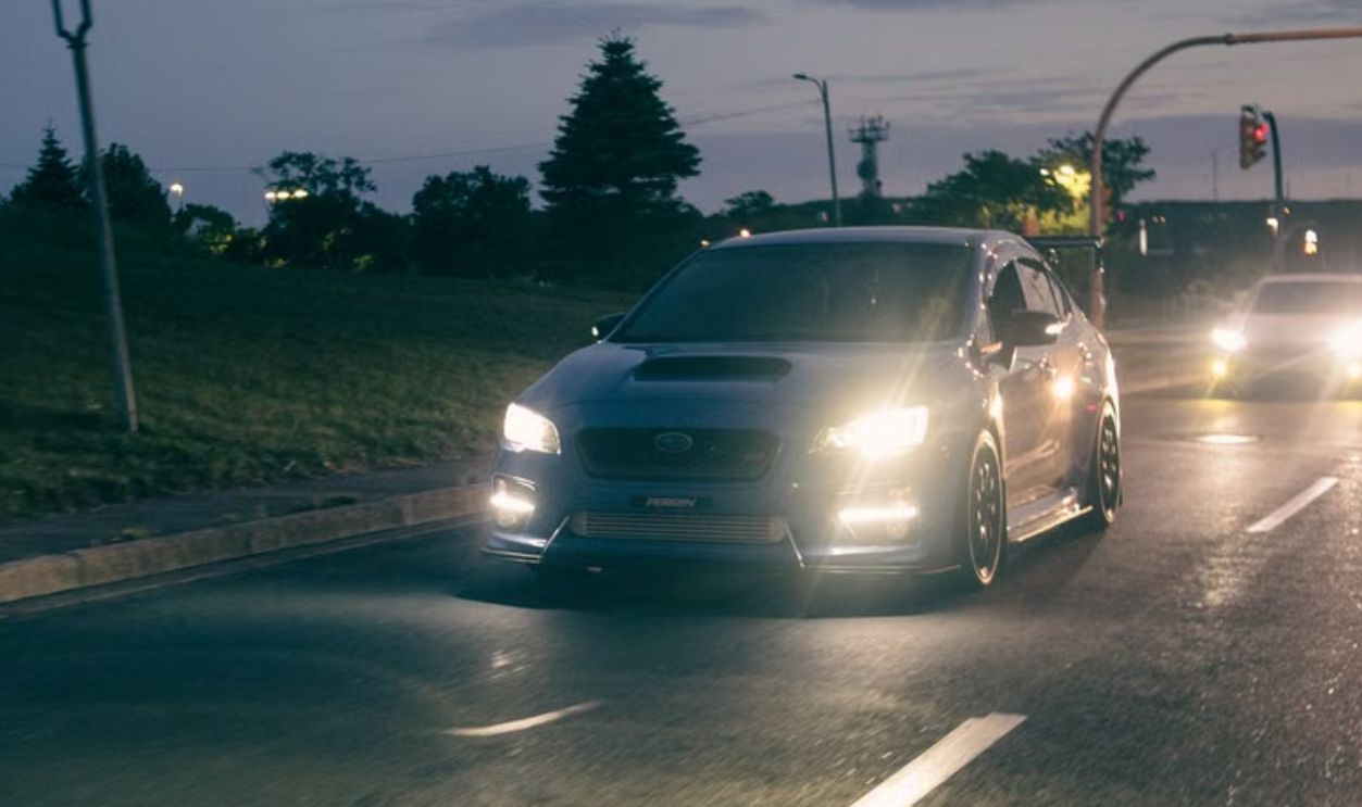 A sleek Subaru WRX drives on a city street at dusk, headlights on, capturing the essence of night travel