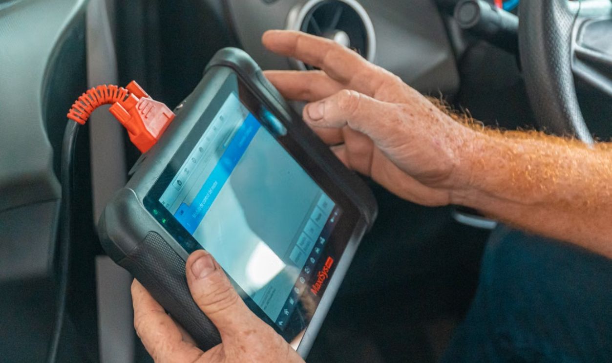 A mechanic uses a diagnostic tablet inside a car for vehicle analysis