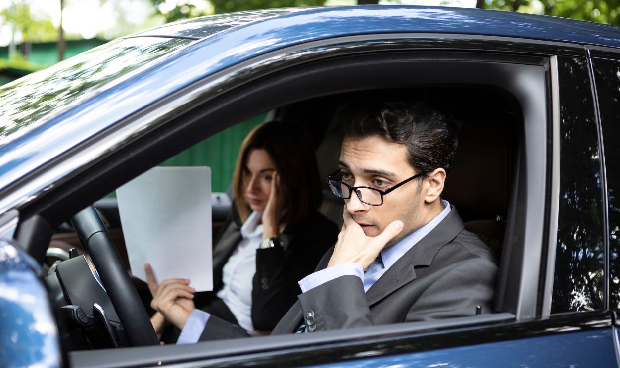 Handsome businessman sitting in his luxury car and holding documents and feeling bad. Bankruptcy and problems at the business concept