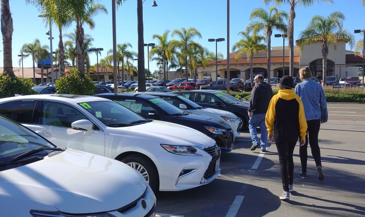 A man and his teen daughters shopping for used cars