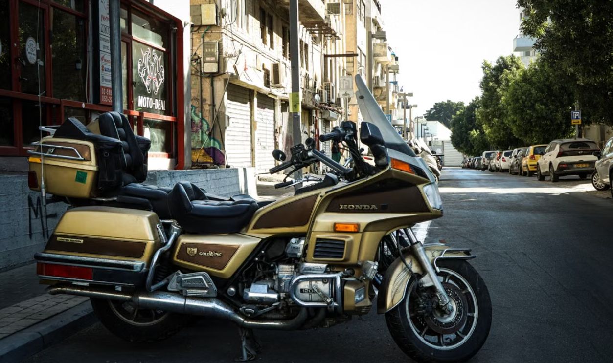 Classic Honda motorcycle parked on a quiet urban street with trees and parked cars.