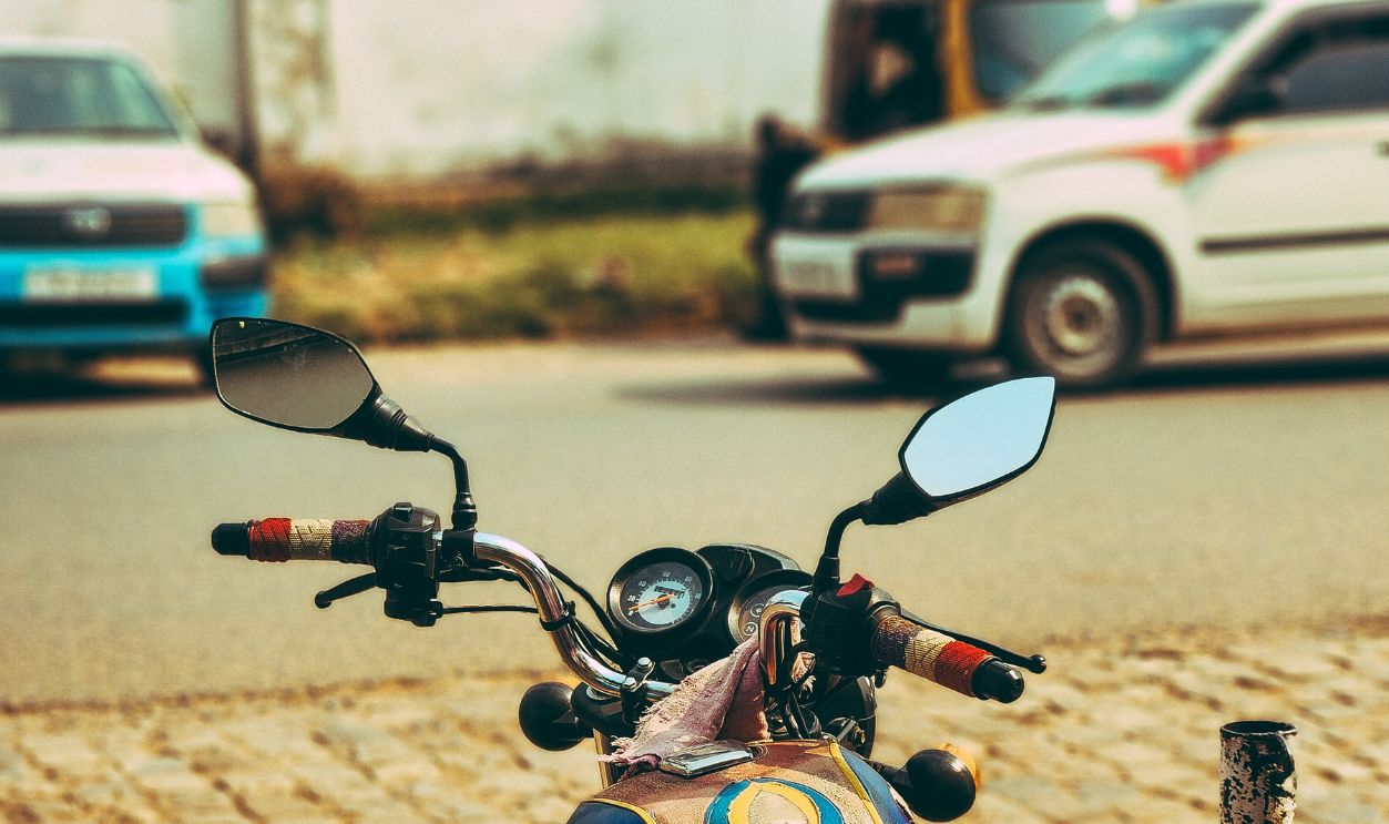 A motorcycle parked on a cobblestone street with vehicles and greenery in the background.