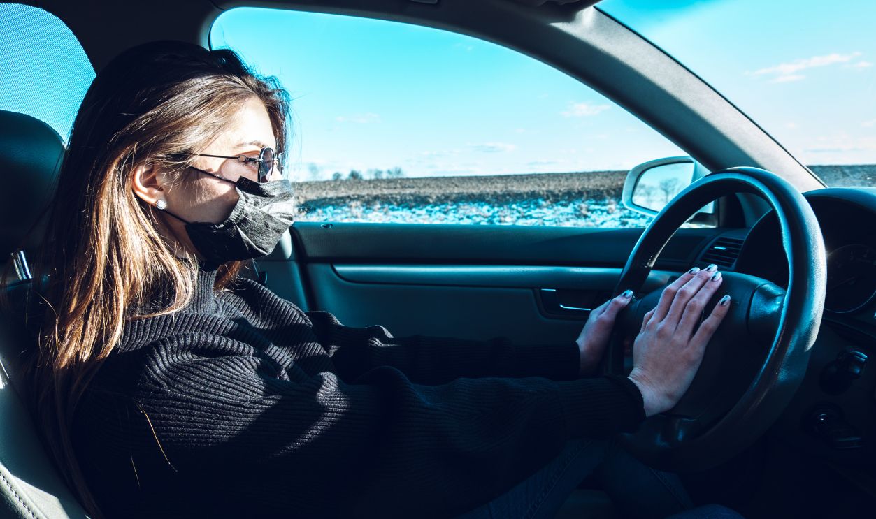 A brunette girl drives a car in a medical mask, fearing infection.