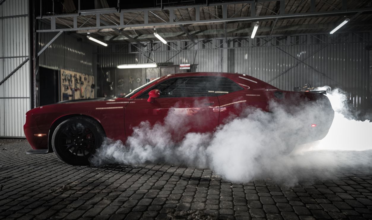 A red car spins its rear tires in a garage. Smoke fills the space as the car creates a loud sound.