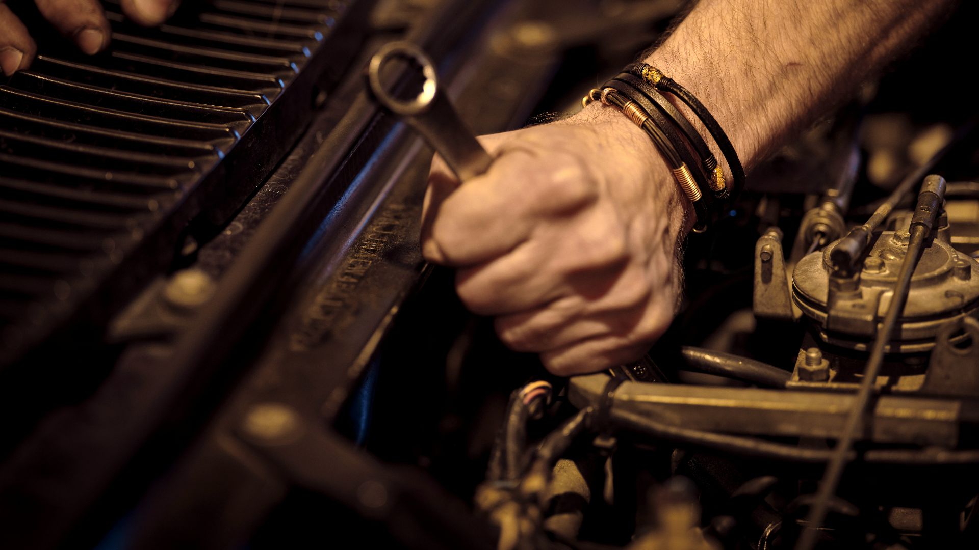 Hands with grease working on a car engine with a metal wrench