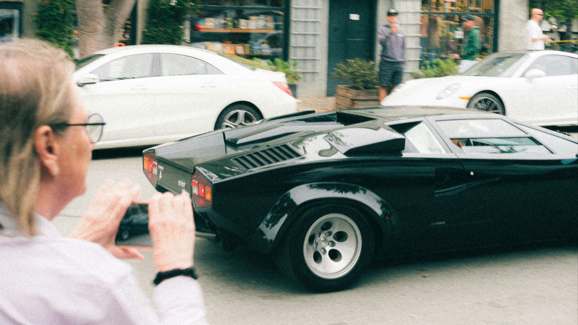 A person photographs a black vintage sports car