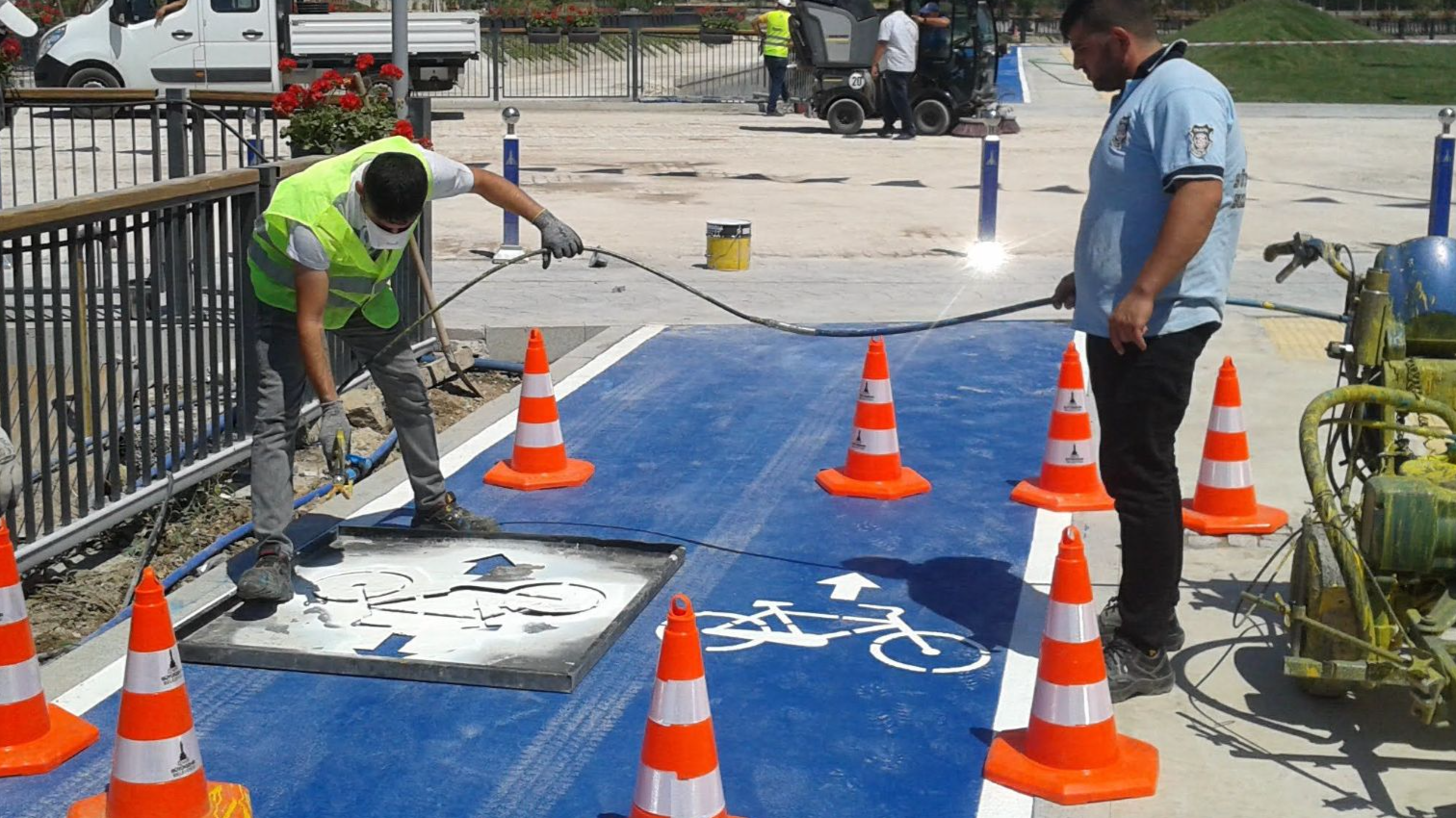 Full body road workers wearing uniforms and high visibility vests marking cycle lane with white paint on sunny weather