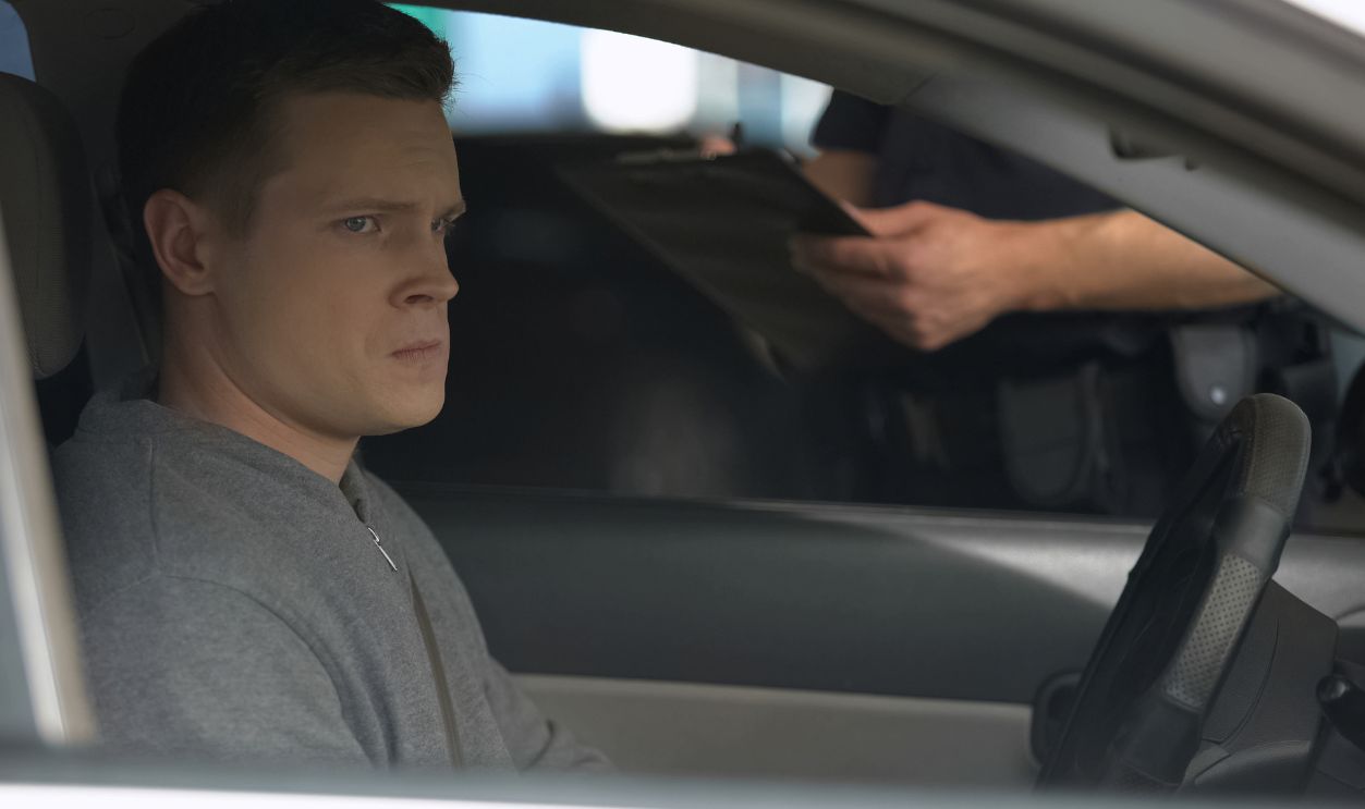 Police officer writing traffic ticket to upset male driver, moving violation