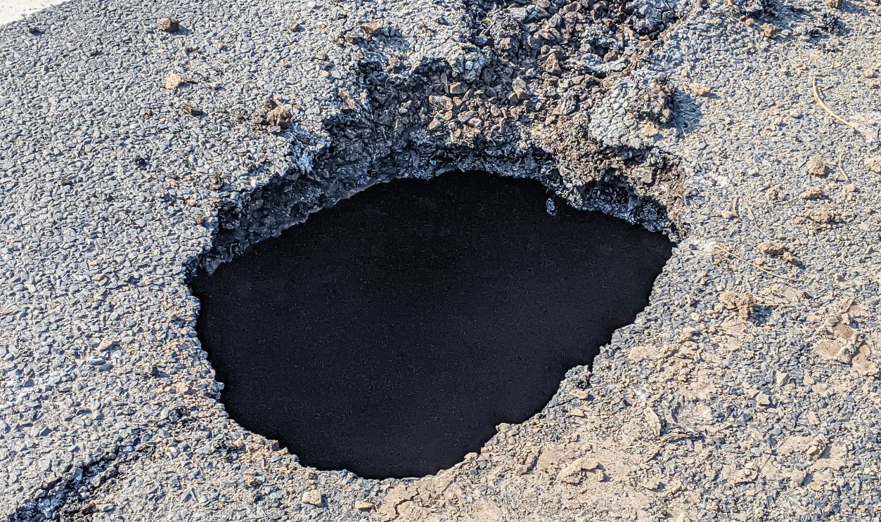 Deep sink hole opened up in a tarmac road surface.