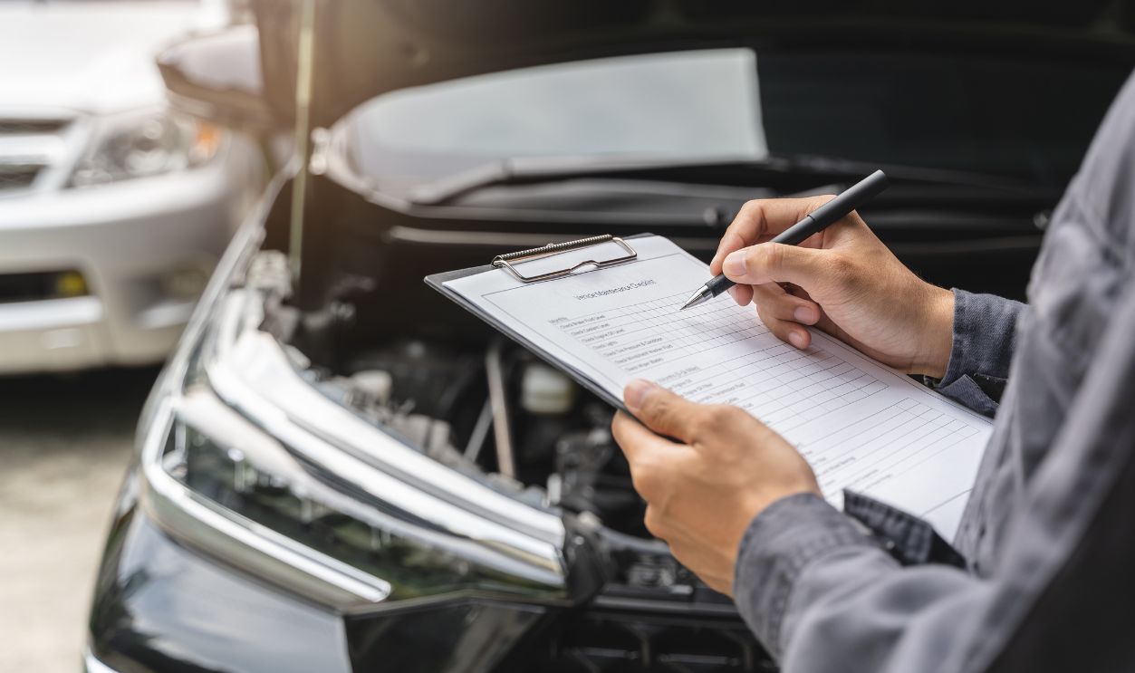 Auto check up and car service shop concept. Mechanic writing job checklist to clipboard to estimate repair quotation to client at workshop garage.