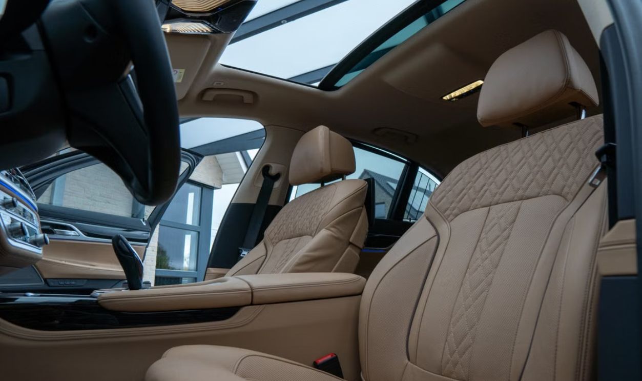 Elegant car interior featuring beige leather seats and a panoramic sunroof, highlighting luxury and comfort.