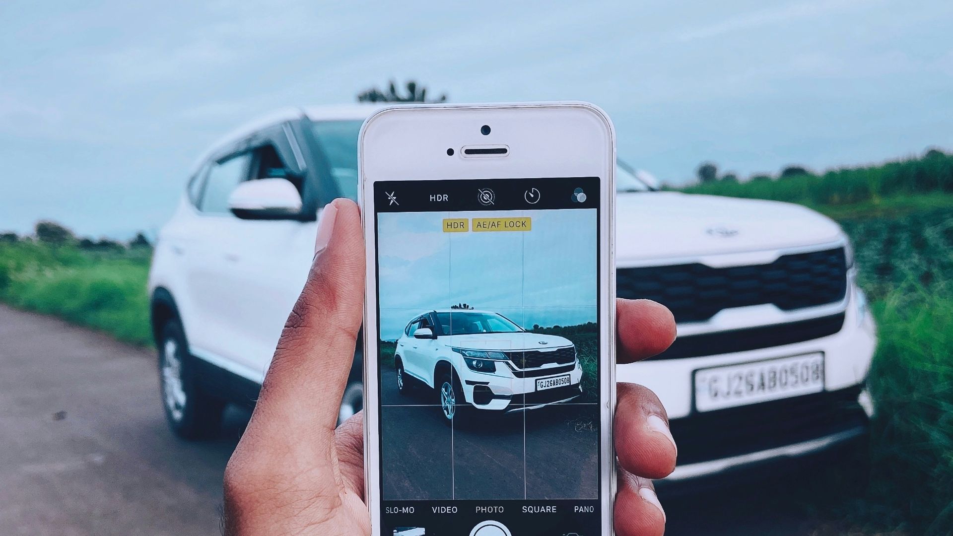 person holding silver iphone 6 taking photo of white car on road during daytime