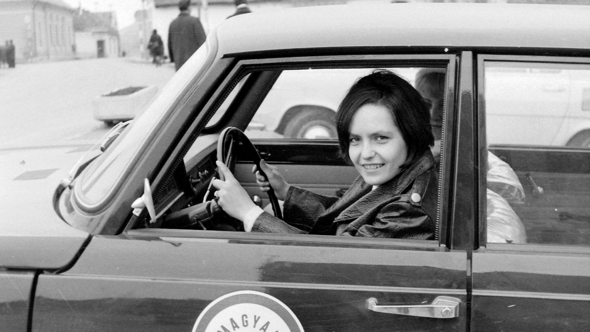 Probably driving lesson, a student in a Hungarian Automobile Club  Wartburg car

Tags: chauffeur, Wartburg-brand, Gerrman brand, automobile, Hungarian Automobile Club
