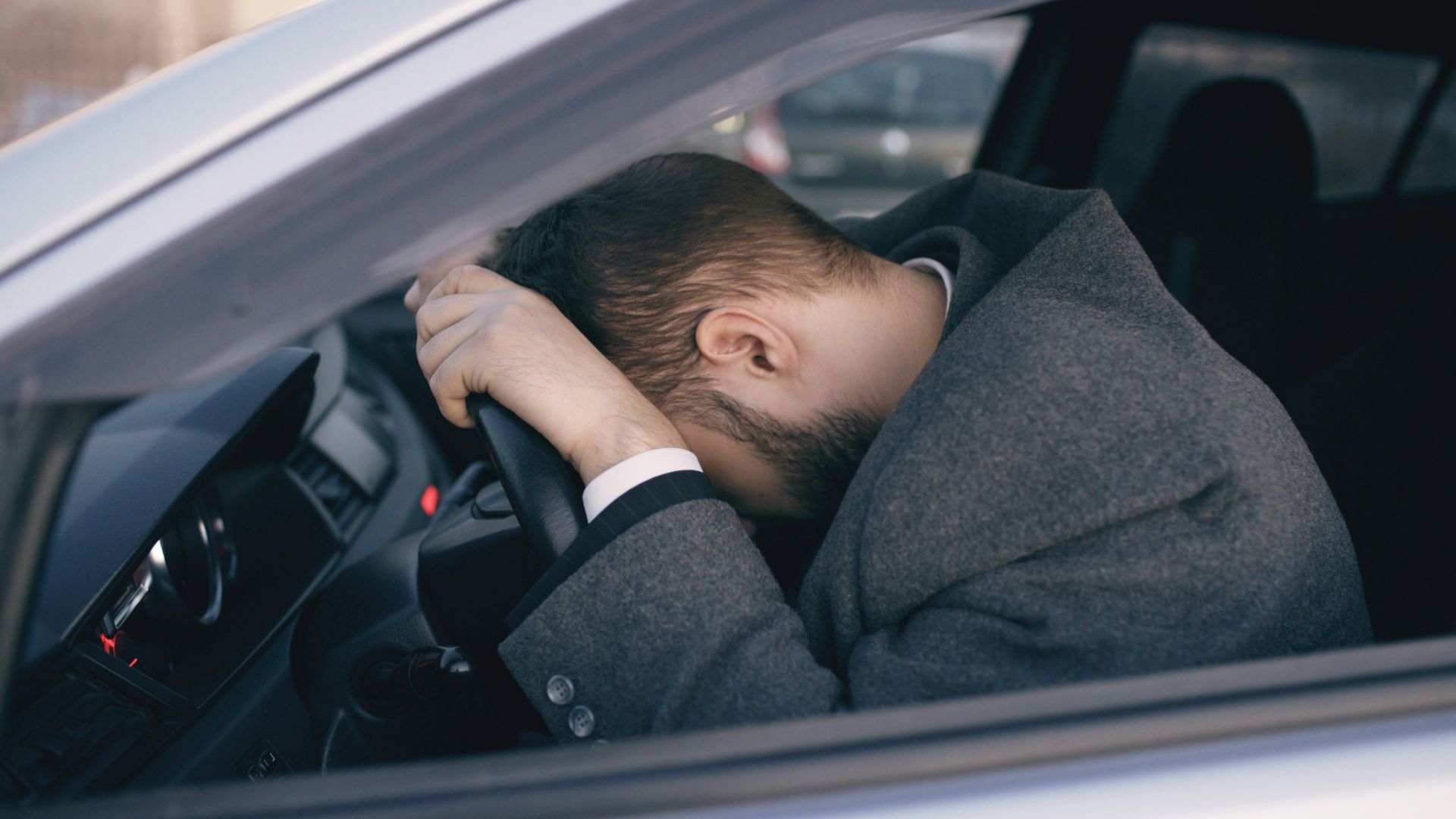 Man resting head on steering wheel inside car