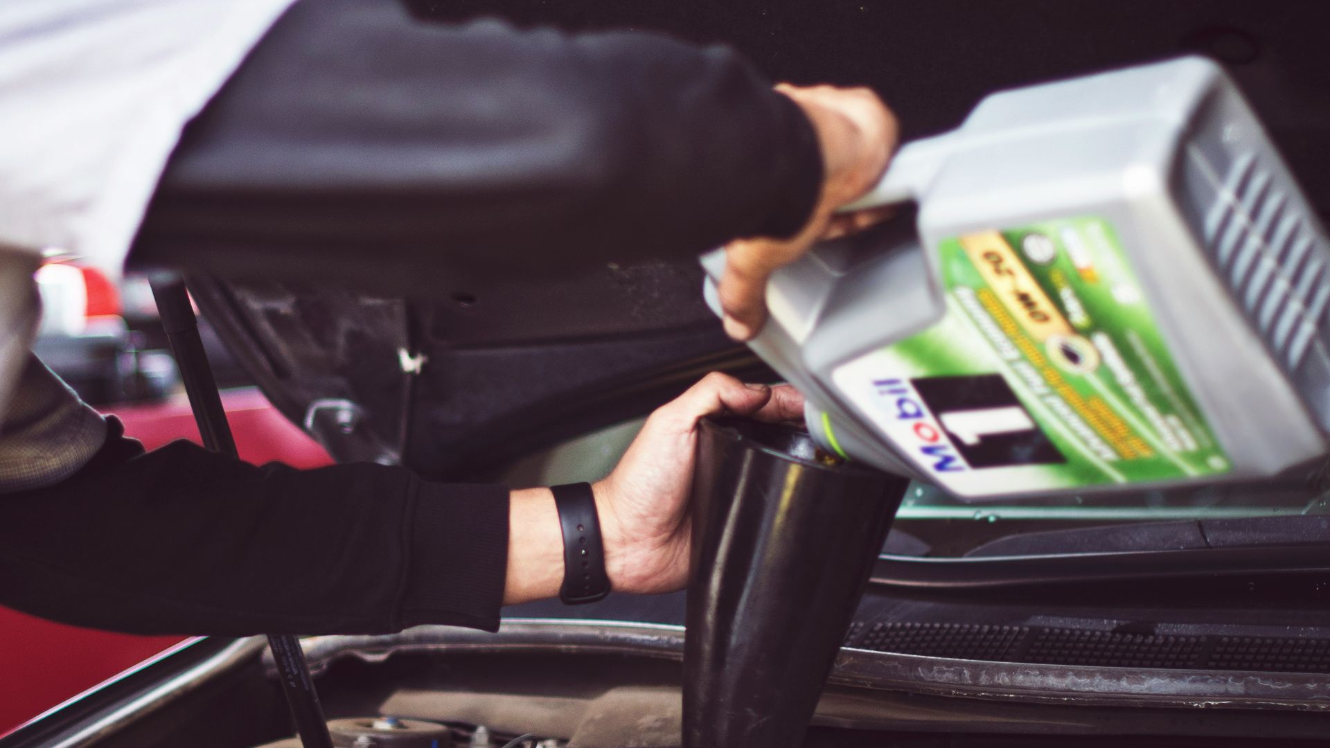 man refilling motor oil on car engine bay