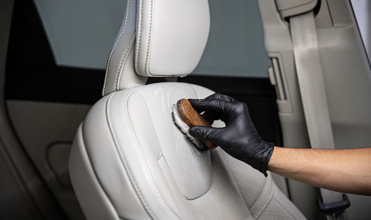 Man car detailing studio worker cleaning car leather seat with a brush.