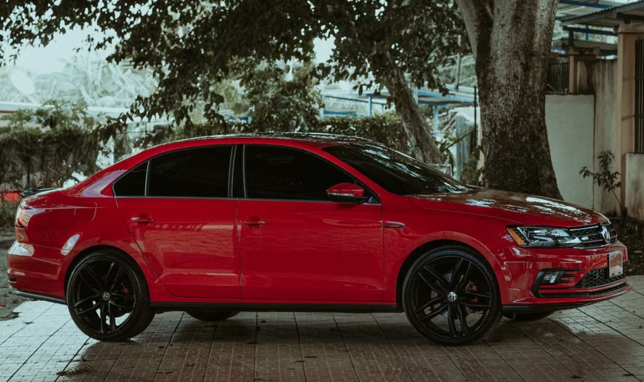 A striking red sedan parked under a tree on a paved surface, exuding style and elegance
