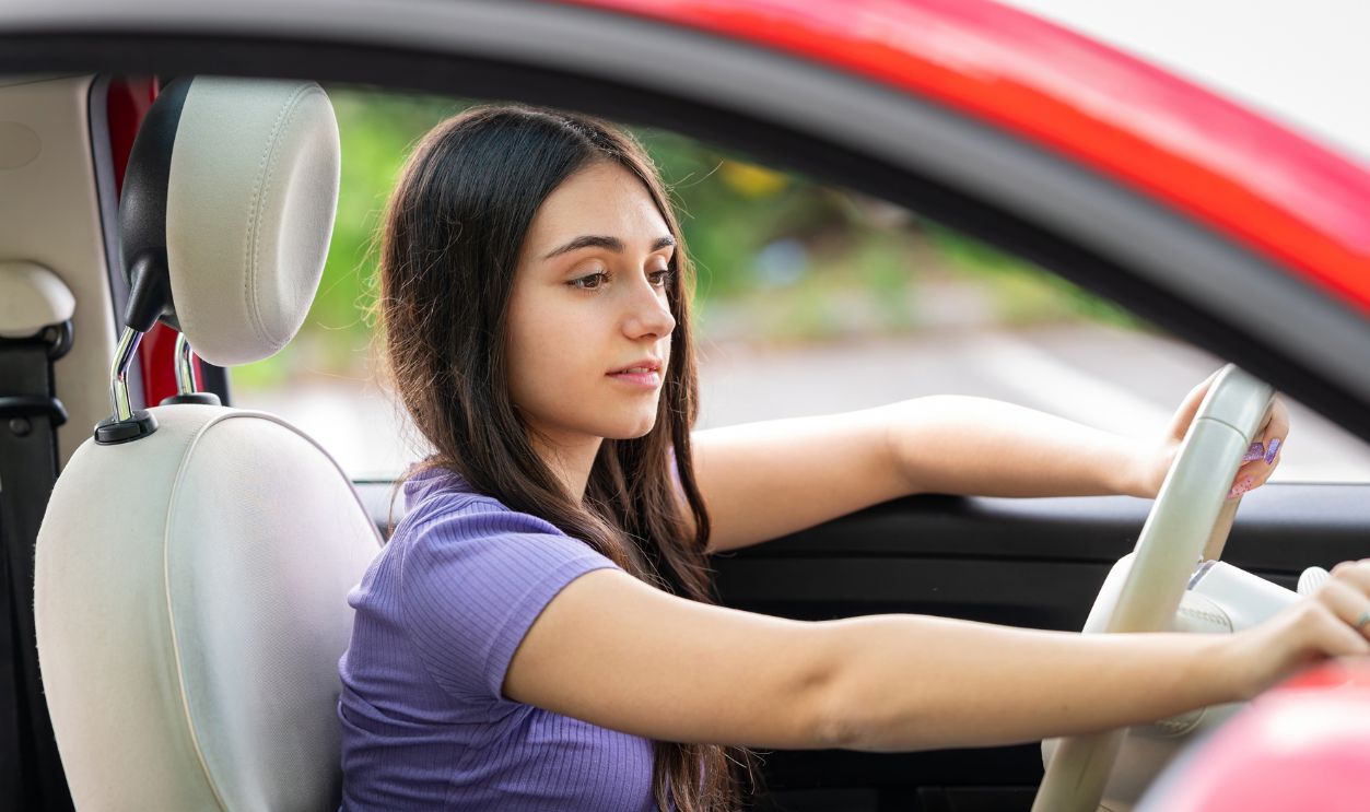 Teenager driving a red car and adjusting the stereo volume