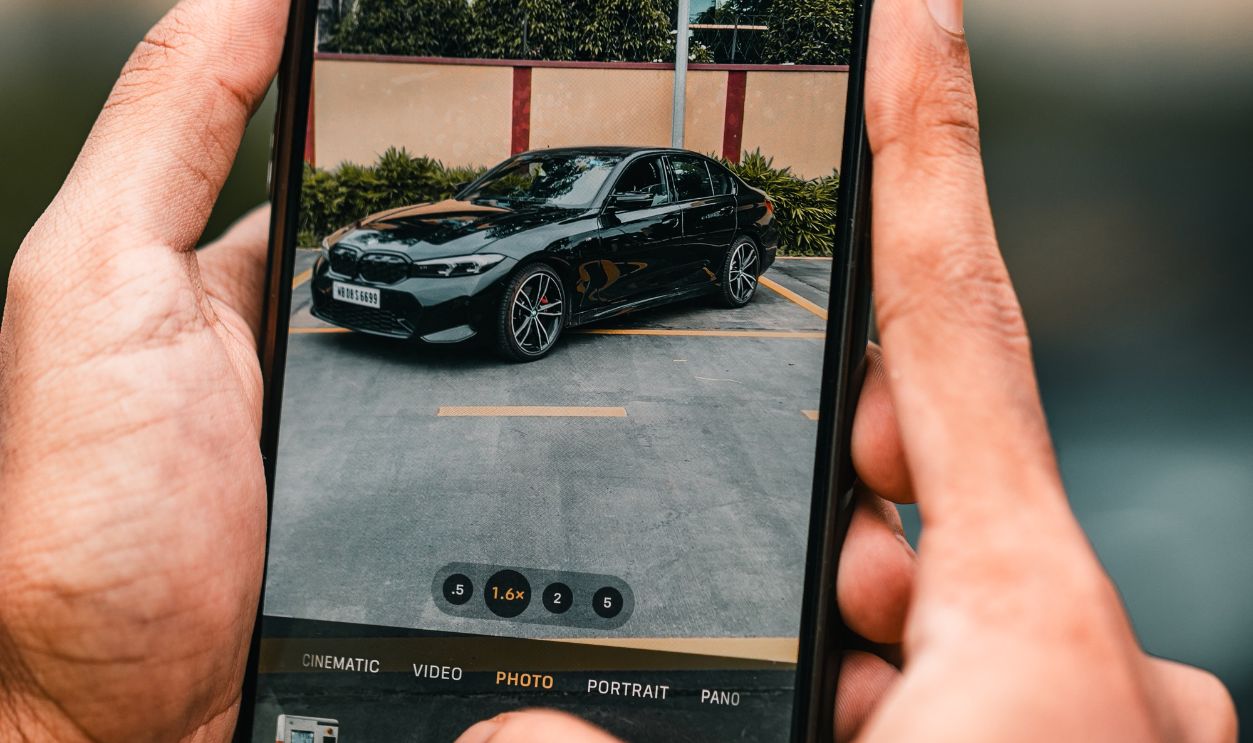 Hands holding a smartphone capturing a car image in a parking lot.