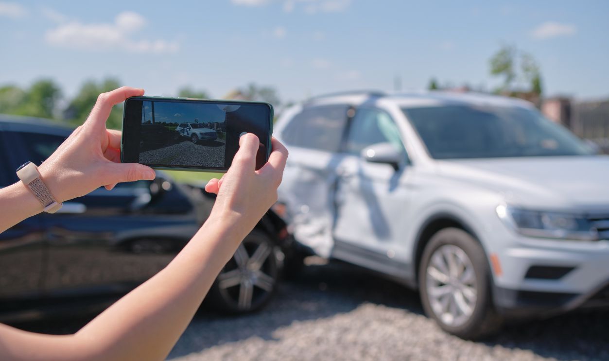 Stressed driver taking picture on sellphone camera of smashed vehicle calling for emergency service help after car accident. Road safety and insurance concept