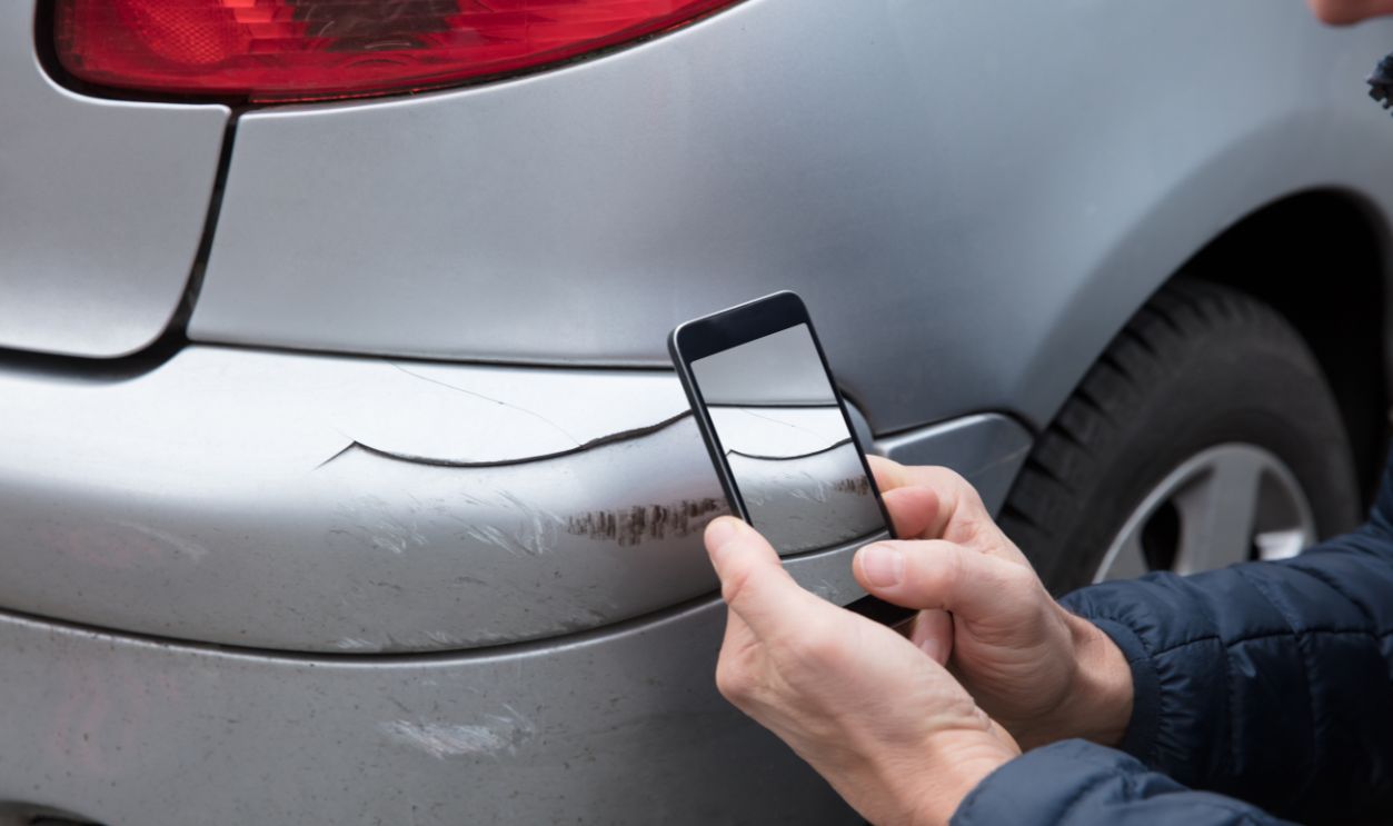 Close-up Of A Person's Hand Taking Photo Of Damaged Car Through Smartphone