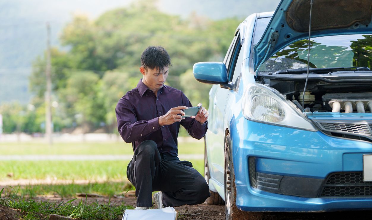 Insurance agent taking photo of broken down blue car for claim report