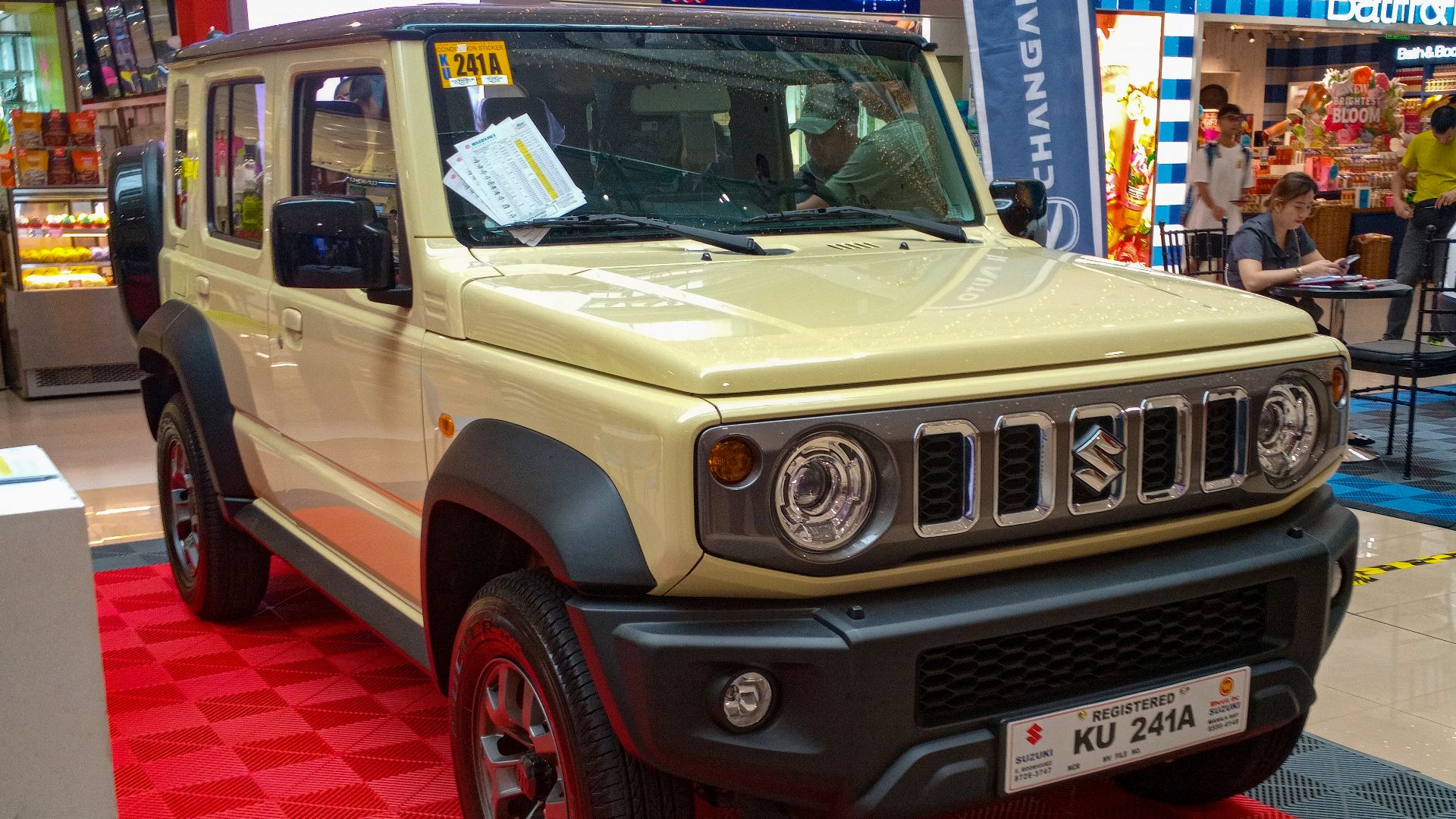 A 2024 Suzuki Jimny 1.5 GLX AllGrip 5dr in Chiffon Ivory Metallic with Bluish Black Pearl roof top, displayed inside SM Megamall.