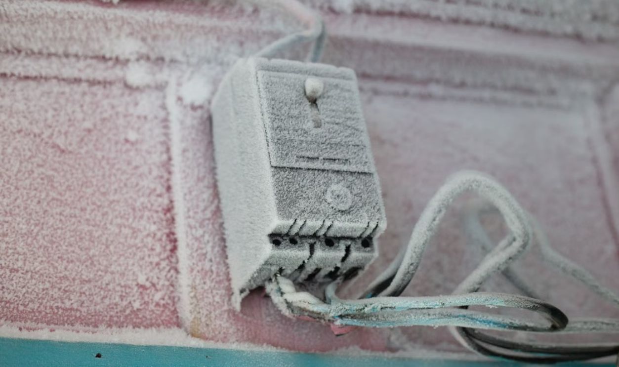 An electrical switch covered in frost and ice during winter on a building's exterior wall.