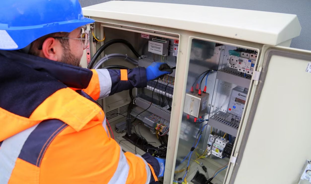Engineer in safety gear working on an outdoor electrical panel, ensuring system functionality.