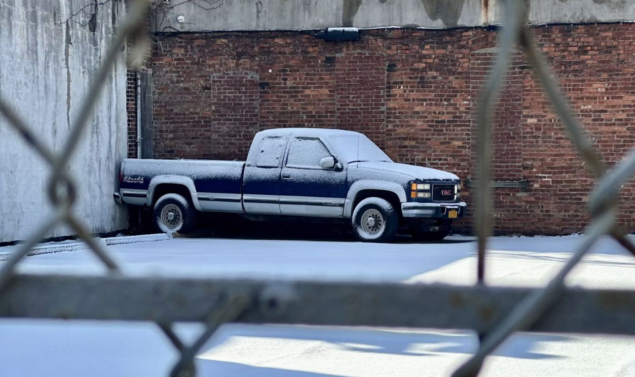A pickup truck covered in snow behind a fence