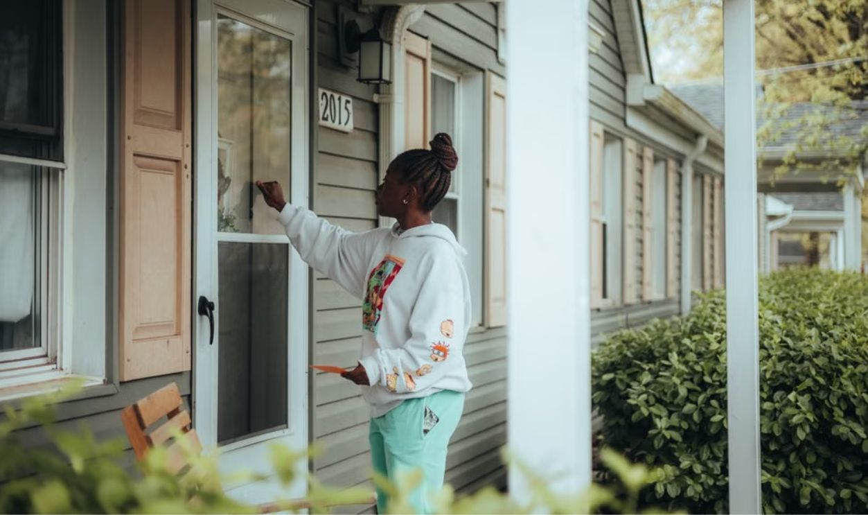 Young woman knocking on a front door in a suburban neighborhood.