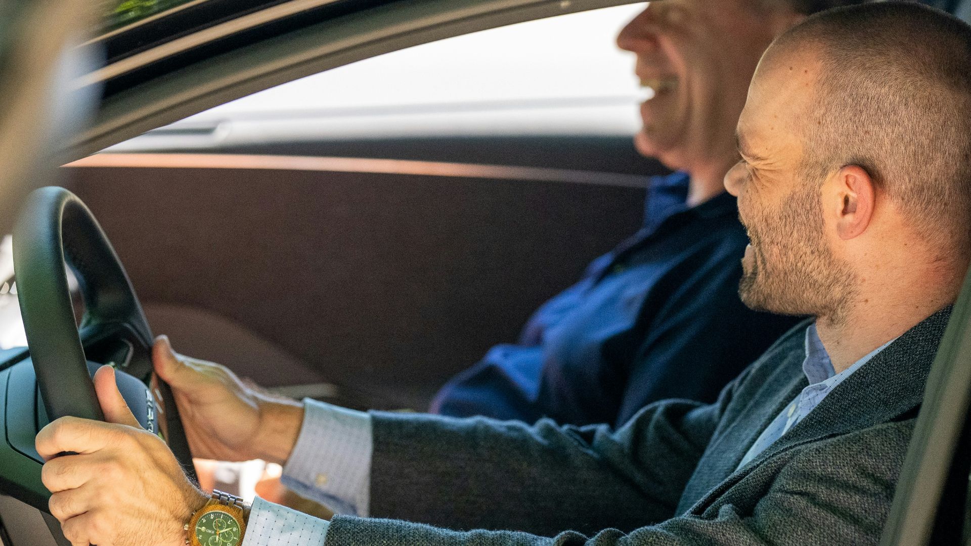 a man driving a car with another man behind him