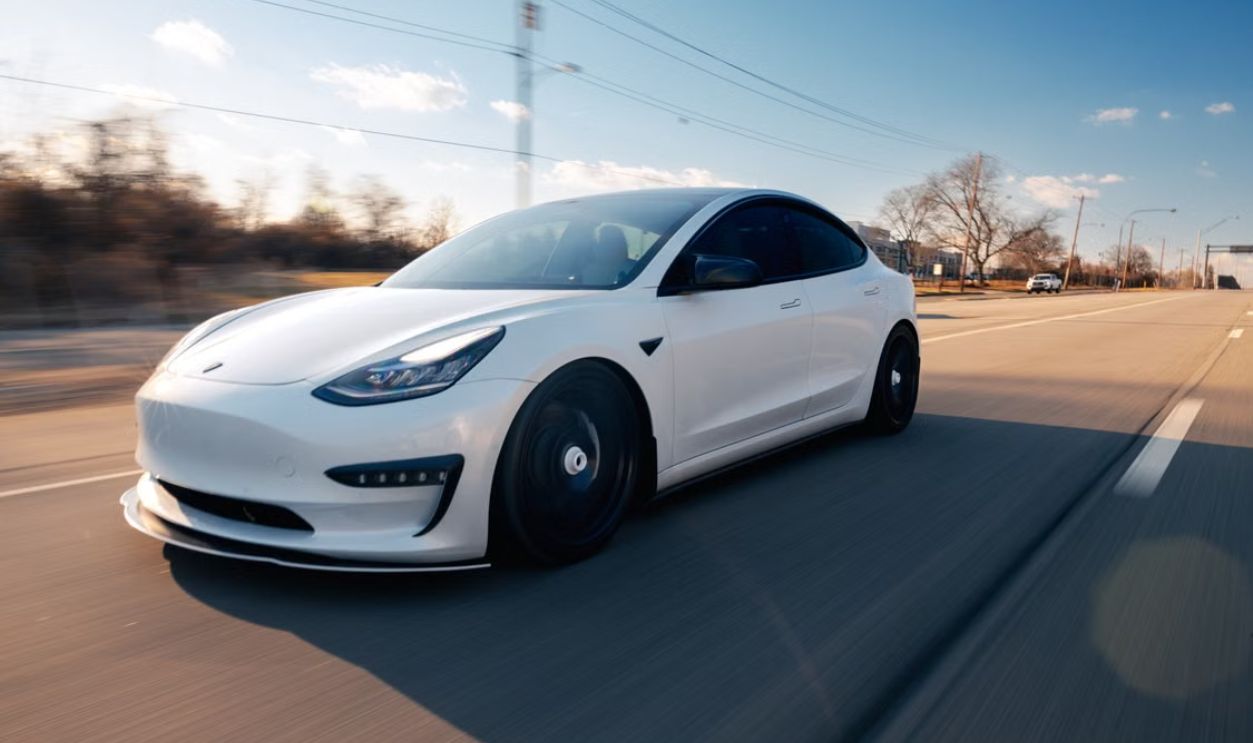 White electric car speeding down a Philadelphia highway on a clear day.