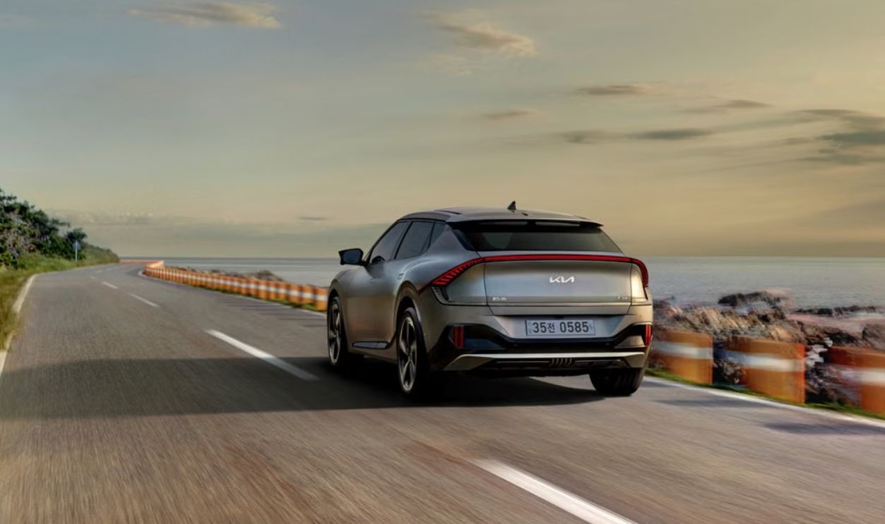Explore the sleek Kia EV6 driving along a picturesque coastal road during sunset.
