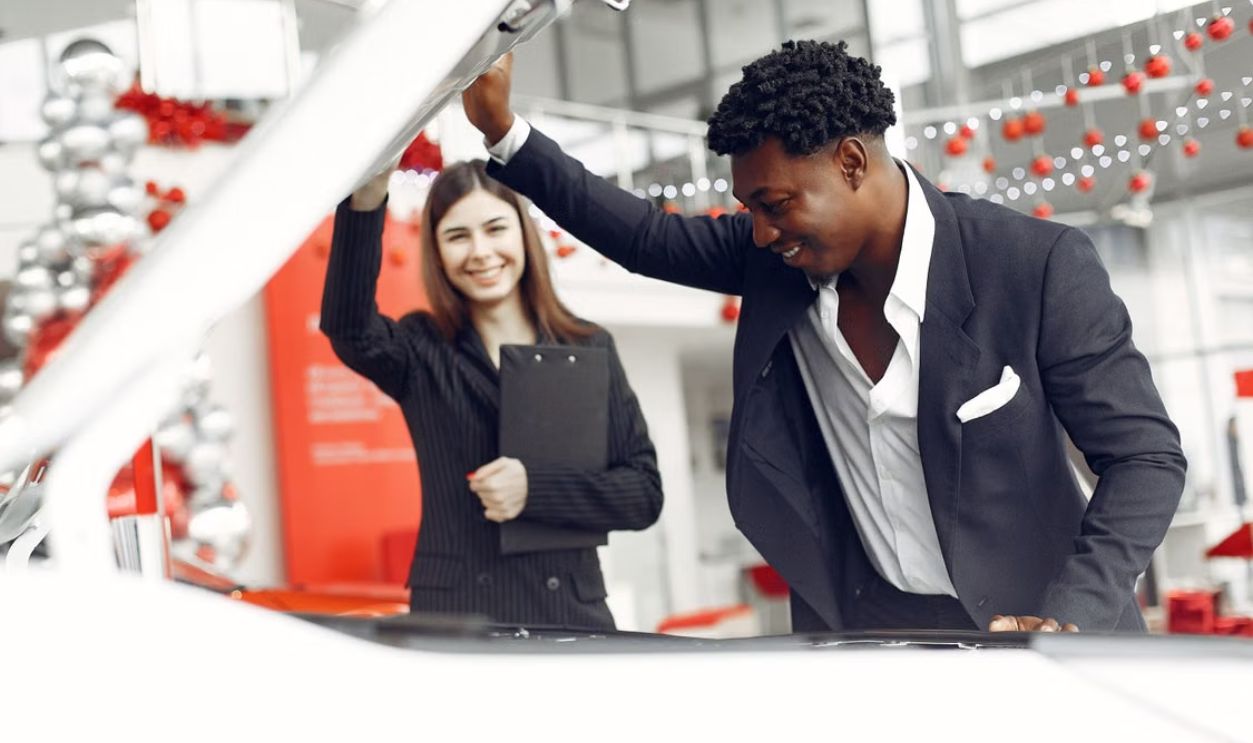 Car dealer and happy customer inspecting vehicle in showroom.