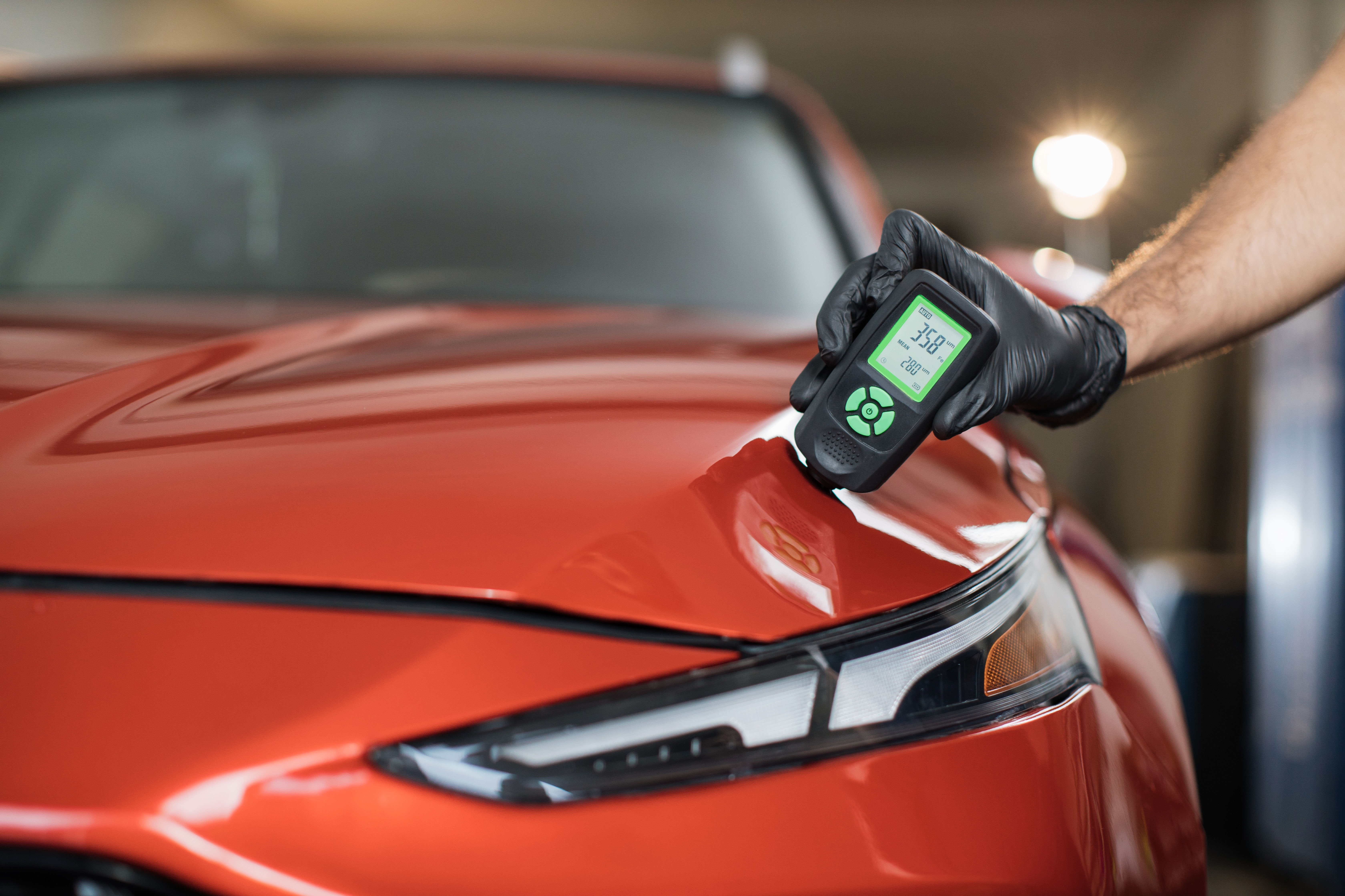 Shutterstock - 2239710273 - Inspector measuring paint cover thickness of red car body at the vehicle detailing service, close-up view on hand and professional thickness meter.