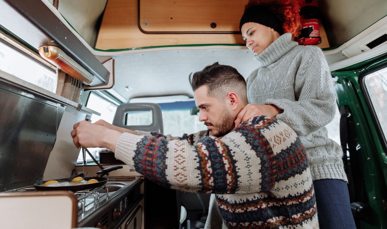 Interracial couple cooking breakfast in cozy camper van during a road trip adventure.