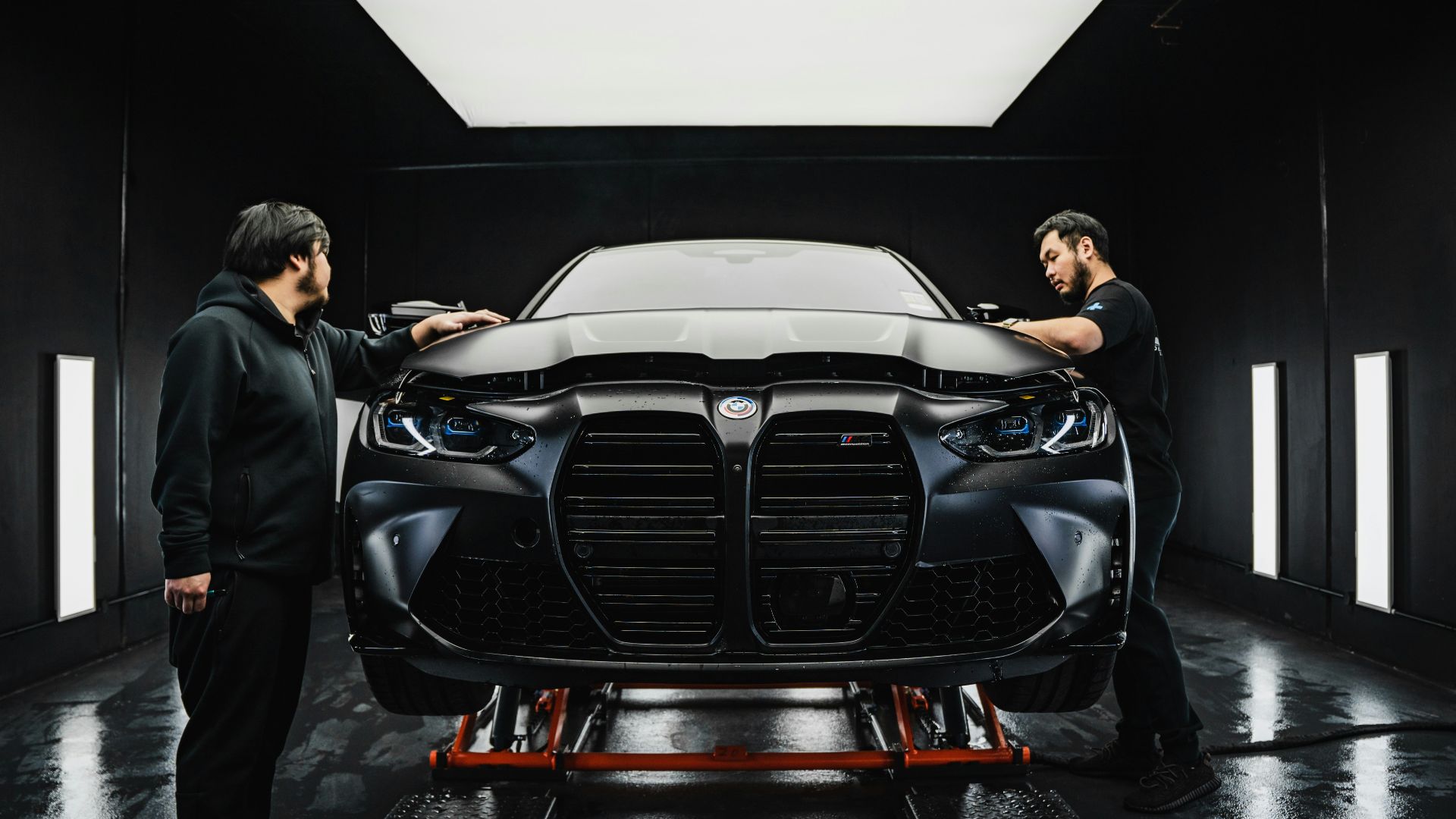 a couple of men standing next to a car in a garage