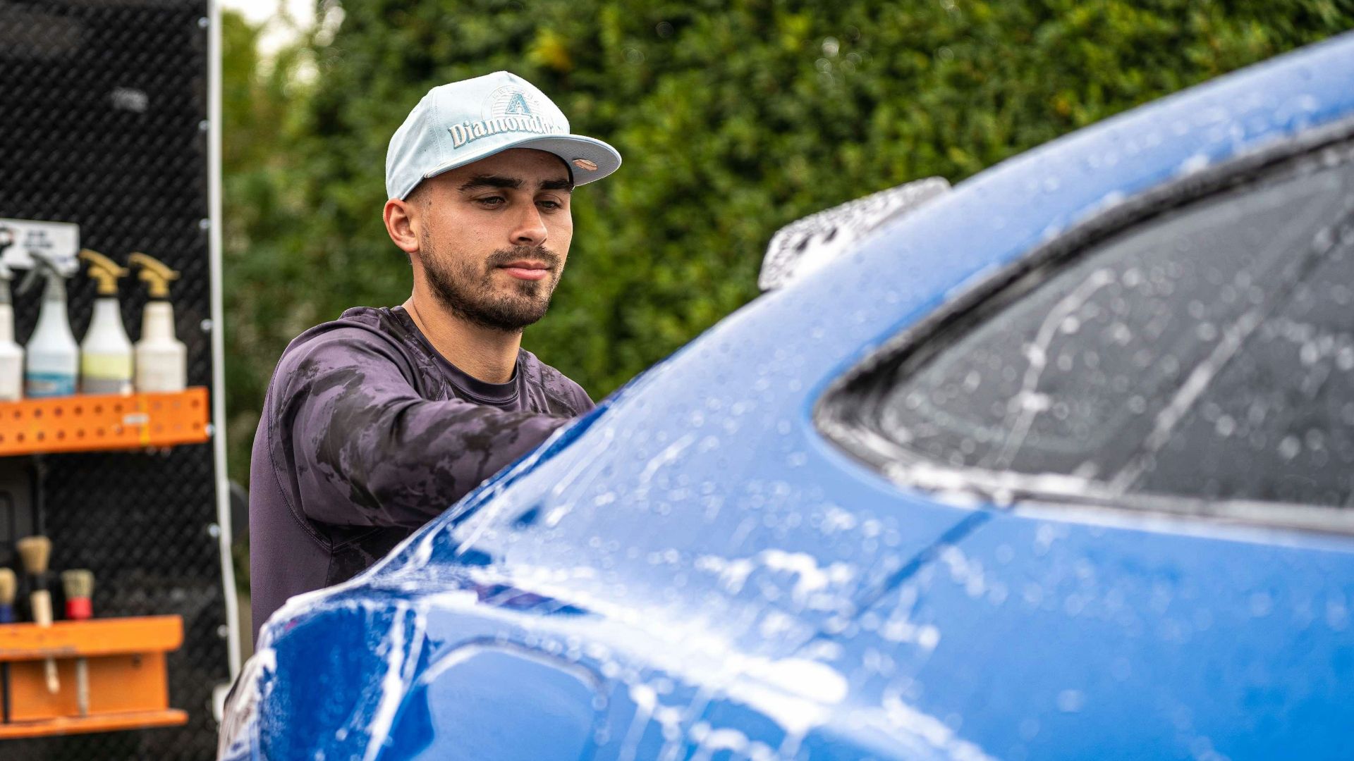 A man washes a blue car with soap