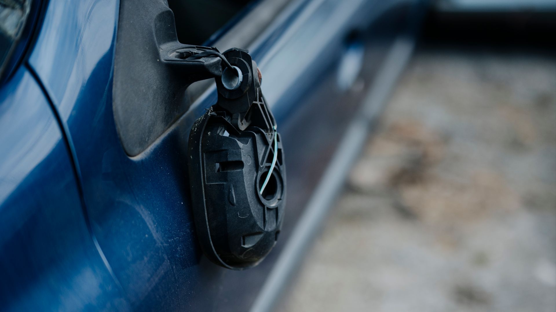A blue car shows a broken side mirror hanging loosely from its door. The setting is a parking area with visible signs of wear on the ground.