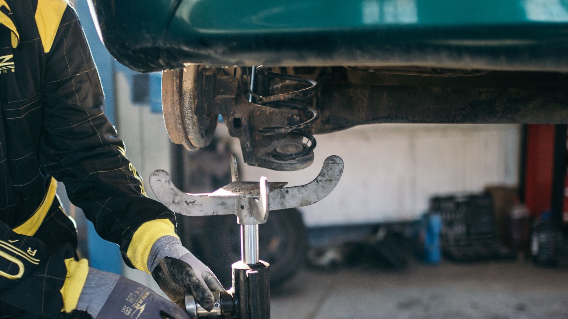 Car mechanic worker repairing suspension of lifted automobile at auto repair garage shop