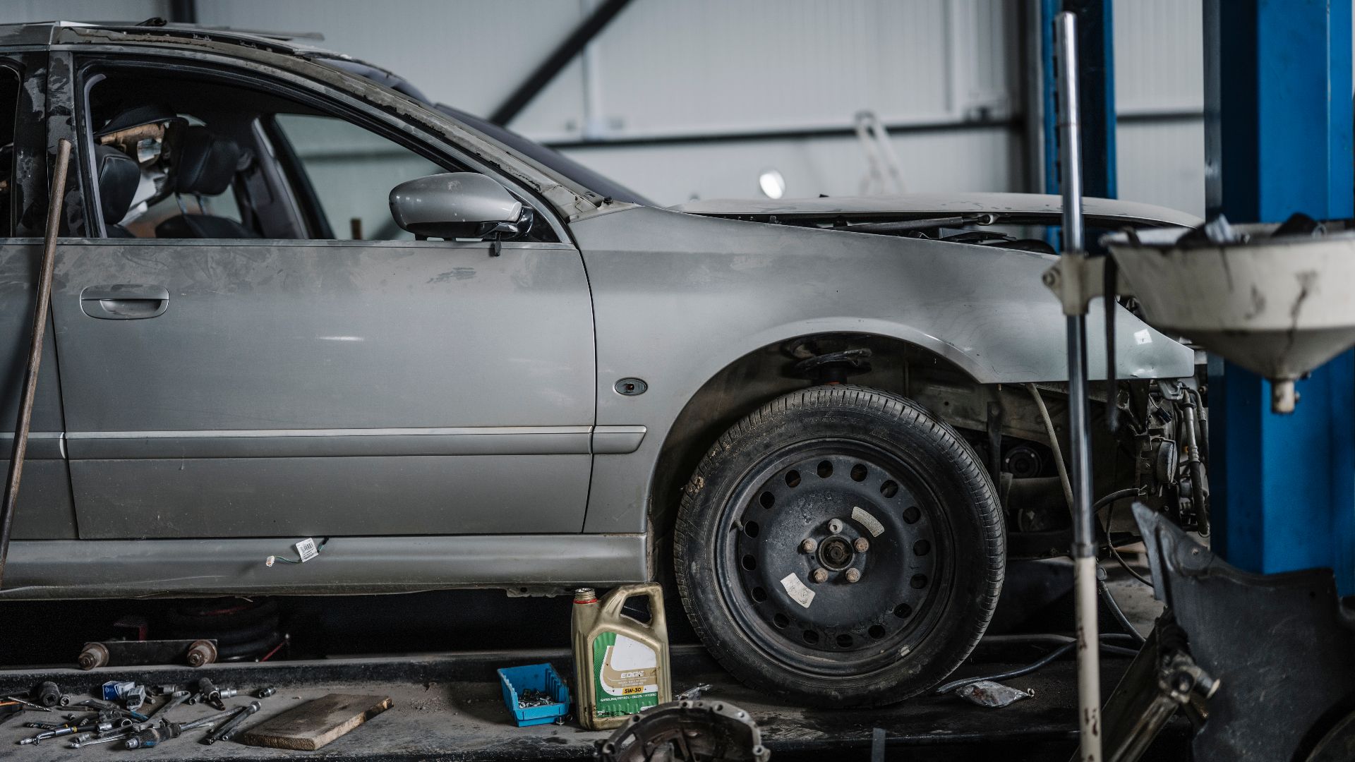 A car is on a lift in an auto shop. Mechanics are working on it while tools and equipment are scattered on the ground. The shop is filled with various items related to car repair.
