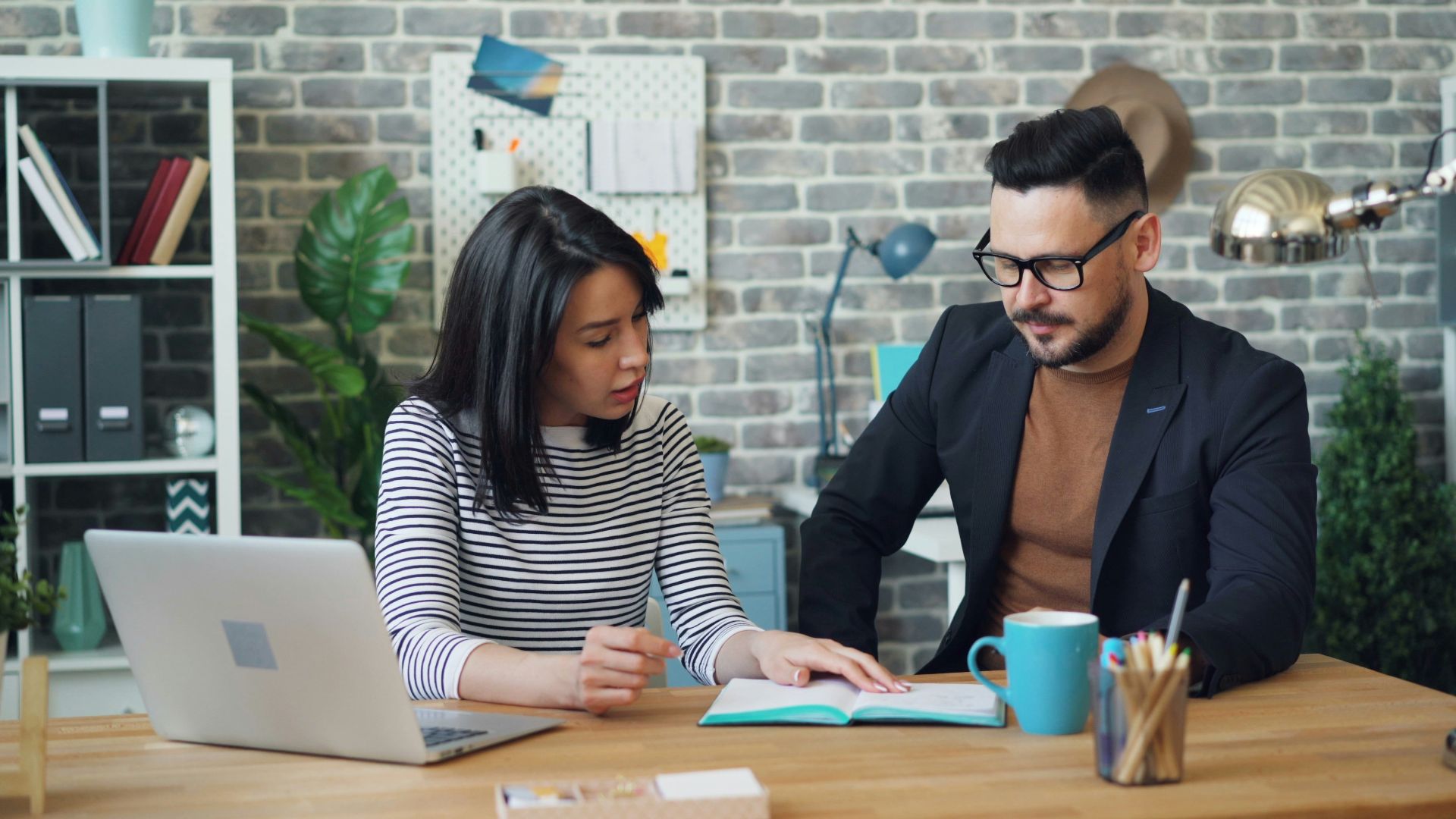 a man and a woman sitting at a table looking at a laptop