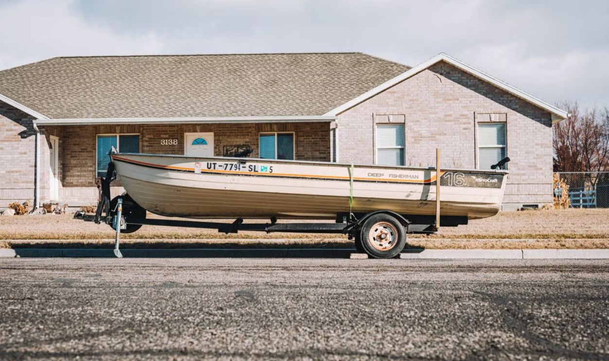 A fishing boat on a trailer parked in front of a suburban house on a clear day